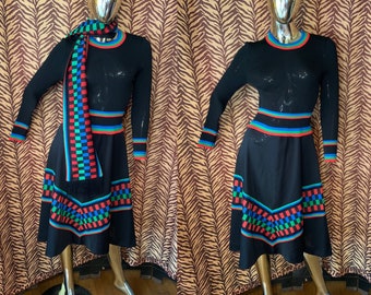 May include: A black knit dress with a geometric pattern in red, green, and blue. The dress has a fitted bodice and a flared skirt. It is paired with a matching scarf.
