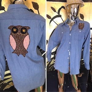May include: A blue denim shirt with a brown and pink owl applique on the back. The owl has yellow eyes and a brown and white checkered pattern on its chest.