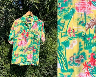 Op de afbeelding: Een geel, kort mouwig overhemd met knopen en een tropische print met palmbomen, zeilboten en mensen. Het overhemd heeft een zak aan de linkerkant en een groen-rood kleurenschema.
