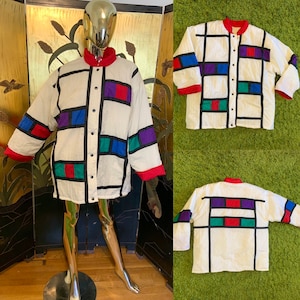 May include: A white quilted jacket with a geometric pattern in red, blue, green, and purple. The jacket has a button-up front and long sleeves.