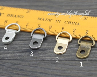 May include: Four different metal D-ring hangers in silver, black, gold, and bronze. The hangers are lined up on a yellow ruler with the numbers 1 through 4 written below each hanger.