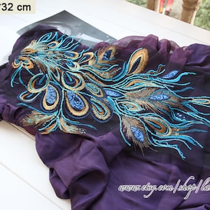 Puede incluir: Tela transparente de color morado con un diseño de pluma de pavo real bordado en hilo azul y dorado. La tela mide 60 cm por 32 cm.