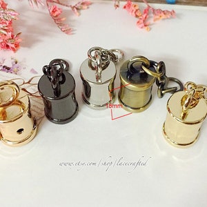 Könnte beinhalten: Vier Metall-Kettenendenkappen in verschiedenen Ausführungen: Gold, Silber, Schwarz und Antik-Messing. Jede Kappe ist 3,8 cm hoch und hat eine runde Form. Die Kappen werden verwendet, um die Enden von Ketten zu veredeln.