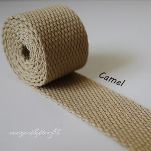 Può includere: Primo piano di un rotolo di fettuccia di cotone color cammello. La fettuccia è tessuta con un motivo testurizzato ed è larga circa 2,5 cm.