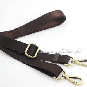 May include: A brown canvas strap with gold-toned hardware, including a buckle and two swivel clasps. The strap is approximately 1 inch wide.