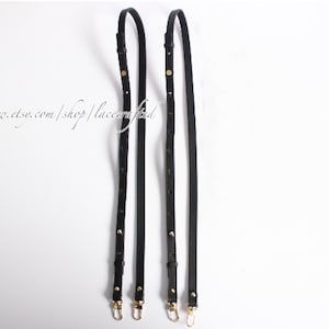 Könnte beinhalten: Zwei schwarze Lederriemen mit goldenen Beschlägen und Nähten. Die Riemen sind etwa 100 cm lang und 2,5 cm breit.