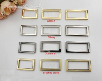 May include: Four rows of metal rectangular rings in different finishes: golden, silvery, gunmetal, and brushed brass.