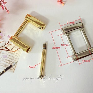 May include: Two metal buckles, one gold and one silver, with measurements in millimetres. The gold buckle is 29 mm long, 18 mm wide, and 3 mm thick. The silver buckle is 21 mm long, 18 mm wide, and 11 mm thick.