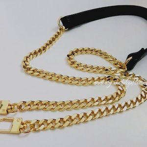 Könnte beinhalten: Ein goldener Kettenriemen mit zwei Verschlüssen und einem schwarzen Lederriemen. Die Kette ist im Curb-Stil.