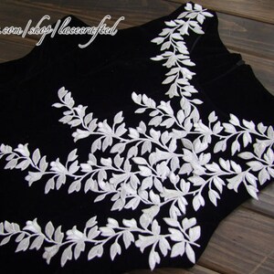 Puede incluir: Tela de terciopelo negro con diseño floral bordado en blanco. El diseño presenta delicadas hojas y flores.