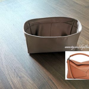 May include: A taupe handbag organiser with several compartments. The rectangular organiser has rounded corners and is designed to fit inside a larger bag. A smaller image shows a brown leather handbag with a top handle and shoulder strap.