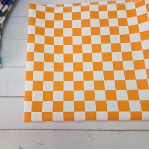Peut inclure: Tissu à carreaux orange et blanc. Le tissu est plié, montrant un motif de carrés espacés uniformément. Le tissu est fait d'une matière tissée et est probablement utilisé pour l'artisanat ou la décoration intérieure.
