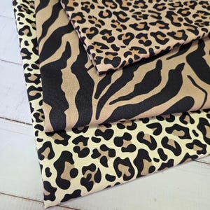 Puede incluir: Primer plano de tres muestras de tela plegadas con estampados de animales. La muestra superior presenta un estampado de leopardo en marrón y negro. La muestra del medio tiene un estampado de cebra en marrón y negro. La muestra inferior tiene un estampado de leopardo en crema y marrón.