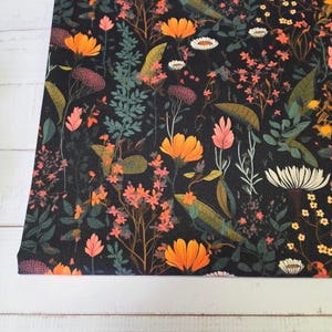 Könnte beinhalten: Ein rechteckiges Stoffpaneel mit einem dichten botanischen Druck auf schwarzem Hintergrund. Das Muster zeigt orange, rosa, weiße und gelbe Wildblumen, durchsetzt mit dunkelgrünem Blattwerk, farnartigen Blättern und verschiedenen Stängeln.
