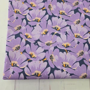 Könnte beinhalten: Nahaufnahme eines Stoffes mit einem sich wiederholenden Blumenmuster. Die Blumen sind ein helles Lila mit gelben und orangefarbenen Zentren, vor einem dunkelblauen Hintergrund. Der Stoff eignet sich für Näh- oder Bastelprojekte.