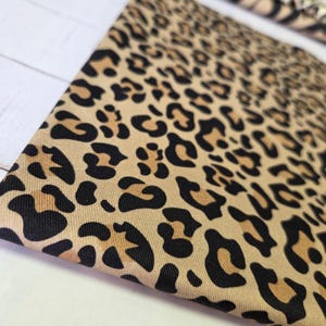 Könnte beinhalten: Nahaufnahme eines beigefarbenen Stoffes mit einem schwarzen und braunen Leopardenmuster. Der Stoff ist gefaltet und zeigt das detaillierte Design des Animal-Prints. Das Muster ist über das gesamte Material gleichmäßig.