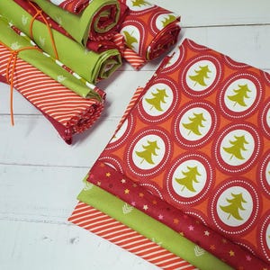 Könnte beinhalten: Eine Sammlung von Stoffstücken mit verschiedenen Mustern, darunter lindgrün mit weißen Chevron-Pfeilen, rot mit weißen diagonalen Streifen und orange mit einem sich wiederholenden Muster aus lindgrünen Tannenbäumen in weißen und roten Kreisen.