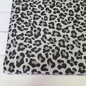 Könnte beinhalten: Ein gefalteter Stoff mit einem Leopardenmuster. Das Muster besteht aus schwarzen und grauen Flecken auf einem hellgrauen Hintergrund. Das Stoffdesign ist ein sich wiederholendes Muster.
