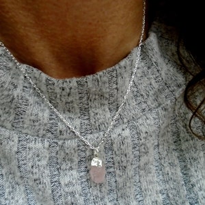 Op de afbeelding: Een zilveren ketting met een lichtroze kristallen hanger.