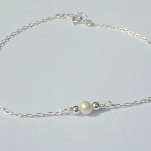 May include: A delicate silver anklet featuring a small, lustrous pearl and two silver beads. The anklet is made of a fine chain and is designed to be worn around the ankle. The pearl is approximately 0.25 inches in diameter.