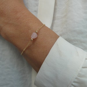 Puede incluir: Un delicado brazalete de cadena dorada con una sola piedra preciosa en forma de corazón rosa claro.