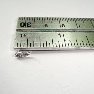 Puede incluir: Un peque&ntilde;o pendiente plateado en forma de ala con piedras transparentes incrustadas. El pendiente est&aacute; colocado junto a una regla, que mide la longitud del pendiente. El pendiente mide aproximadamente 1,3 cm de largo.