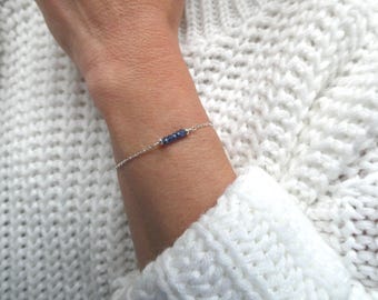 May include: A delicate silver chain bracelet featuring a small row of five tiny, faceted dark blue sapphire beads centered on the wrist. The bracelet is constructed with a thin, polished silver link chain and a secure clasp mechanism.