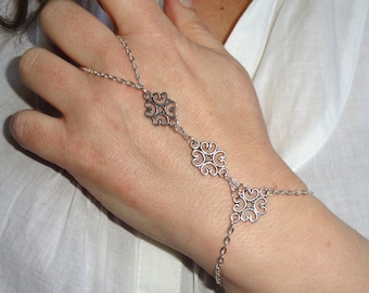 May include: A silver chain bracelet with three decorative charms. The bracelet is connected to a ring that can be worn on the finger.