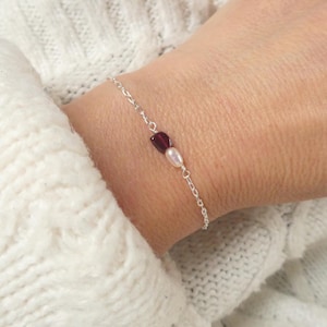 Peut inclure: Un bracelet à chaîne fine en argent orné d'une perle de grenat rouge foncé et d'une perle d'eau douce blanche, reliées par de fins maillons en fil d'argent, formant un bijou épuré et délicat pour le poignet.