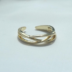 May include: A gold-toned metal ring featuring an open, adjustable band design with multiple thin, polished strands that cross over each other in the centre, creating a delicate, layered appearance with a smooth, reflective surface finish.