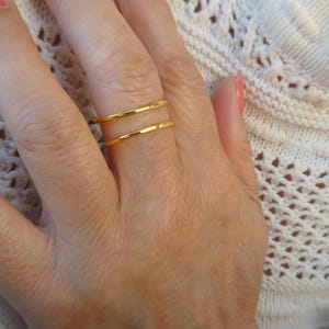 Könnte beinhalten: Zwei dünne, polierte Goldringe an einem Finger. Die Ringe haben ein glattes, abgerundetes Profil mit einer hochglänzenden metallischen Oberfläche. Diese schlichten Ringe werden übereinander getragen und zeigen einen hellen Gelbgoldton.