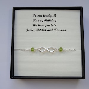 Peut inclure: Un bracelet en argent avec un charme infini et des perles de pierres précieuses vertes. Le bracelet est dans une boîte cadeau noire avec une carte qui dit "To our lovely M Happy birthday We love you lots Jodie, Mitchel and Kai xxx"