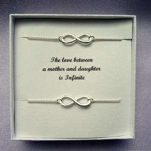 May include: Two silver infinity symbol bracelets in a white box with the text "The love between a mother and daughter is Infinite".
