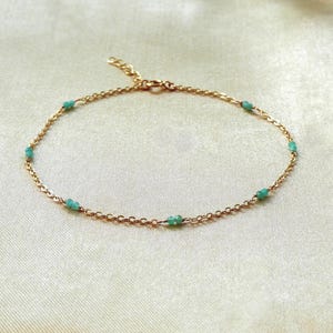 Può includere: Un delicato bracciale a catena dorata con piccole perline color turchese distanziate uniformemente. Il bracciale presenta una sottile catena in metallo con chiusura a moschettone e una catenella di estensione regolabile.