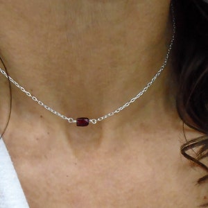 Peut inclure: Un collier en chaîne argent avec un petit pendentif en pierre rouge foncé.