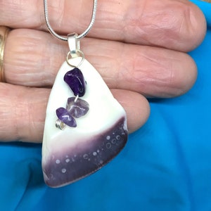 May include: A silver chain necklace with a pendant made from a white and purple seashell with three amethyst stones attached.