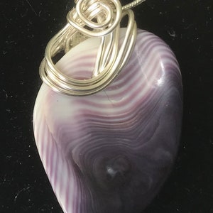 May include: A purple and white shell pendant with a silver wire wrap. The shell has a swirling pattern.