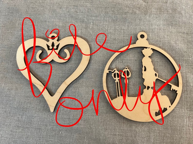 May include: Two wooden ornaments, one shaped like a heart with a crown inside and the other a circle with a character holding a keyblade and two keyblades in the background.