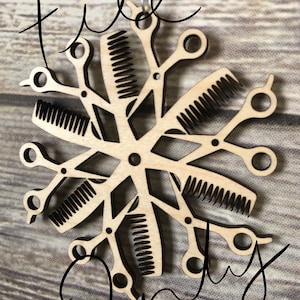 May include: A wooden snowflake ornament with a design of combs and scissors. The ornament is made of light brown wood and has a silver string for hanging.
