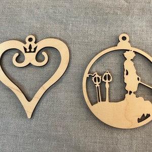 May include: Two wooden ornaments, one shaped like a heart with a crown and the other a circle with a silhouette of a person holding a keyblade.