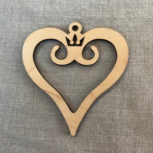 May include: A wooden heart-shaped ornament with a crown design in the center. The ornament is made of light brown wood and has a smooth finish.