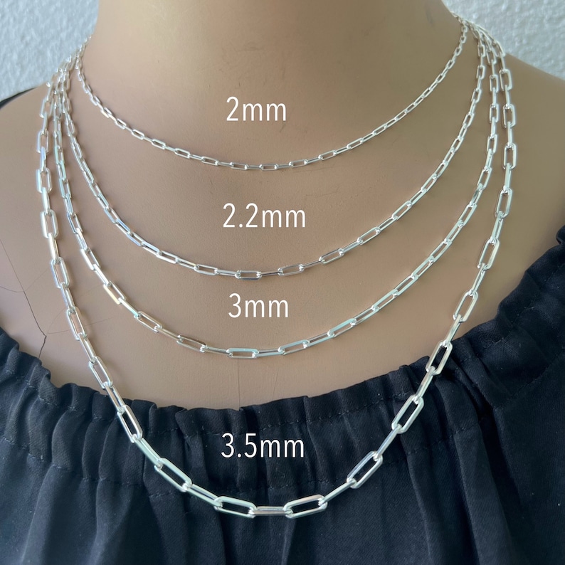May include: Four silver chain necklaces of different sizes, 2mm, 2.2mm, 3mm, and 3.5mm, are displayed on a model's neck. The chains are made of small, rectangular links.
