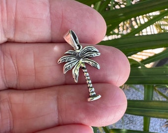 May include: A silver palm tree charm pendant. The palm tree is detailed with textured leaves and a textured trunk.