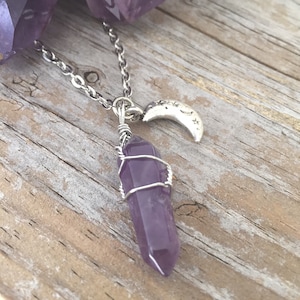 May include: A silver chain necklace with a purple amethyst crystal wrapped in silver wire and a silver crescent moon charm with stars.
