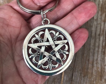 May include: Silver key chain with a pentagram charm. The pentagram is surrounded by a circle of fleur-de-lis designs.