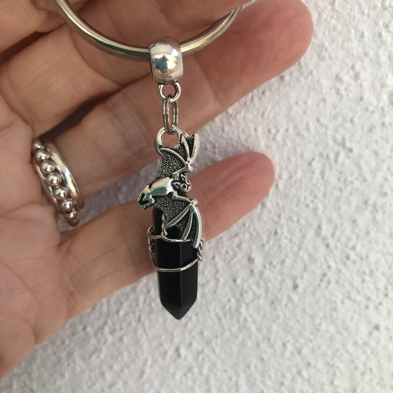 May include: A black crystal point with a silver bat charm attached to a silver key ring.