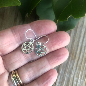 May include: A pair of silver earrings with a pentagram design. The earrings are small and delicate, and they would make a great gift for a witch or pagan.