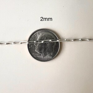 May include: A silver chain necklace with a 2mm width, shown next to a US dime for scale.