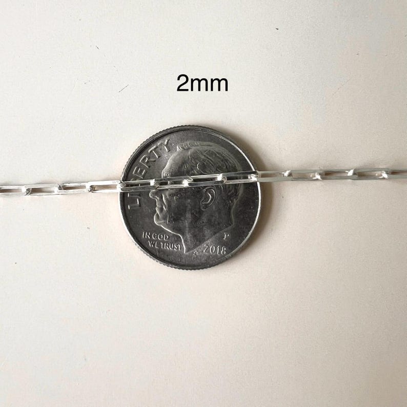 May include: A silver chain necklace with a 2mm width, shown next to a US dime for scale.