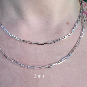 May include: Two silver chain necklaces, one with a 3mm width, layered on a person's neck. The chains are made of small, rectangular links.